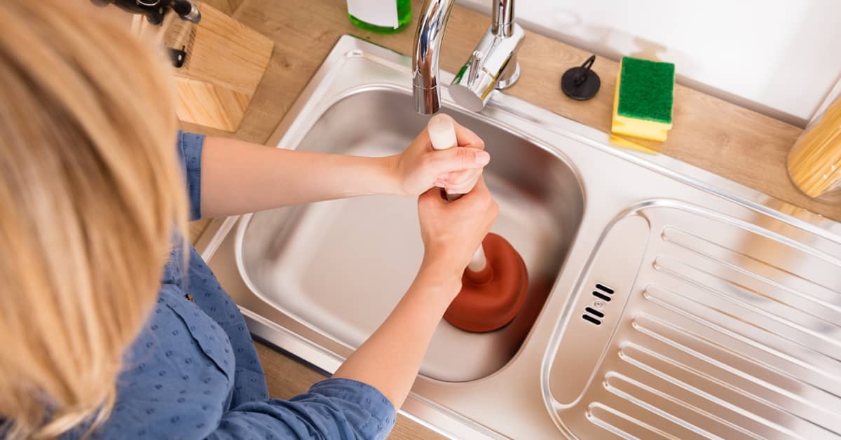 Homeowner using a plunger to unclog a kitchen sink effectively