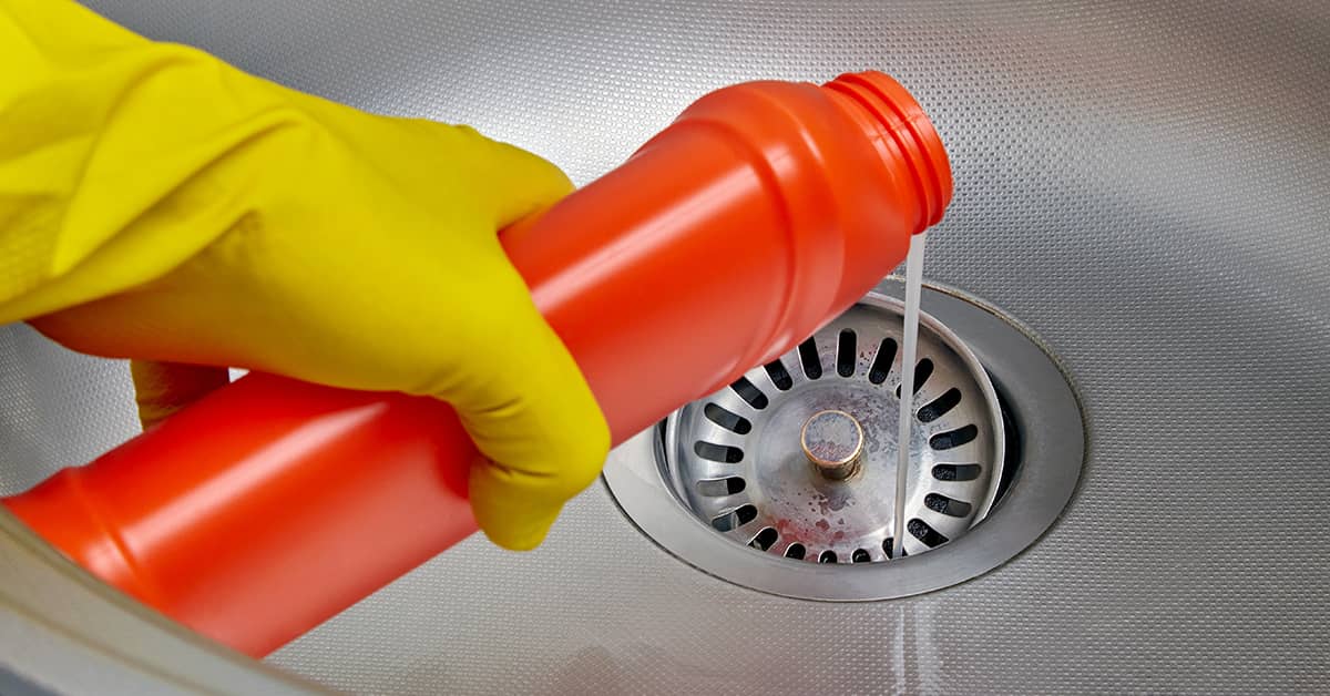 Person pouring chemical cleaner into a kitchen sink drain to clear a blockage.