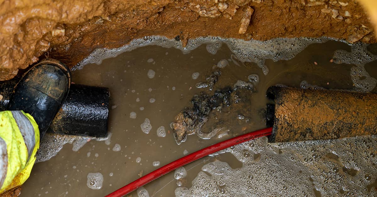 A visibly damaged drain pipe exposed in a trench, illustrating severe structural failure.