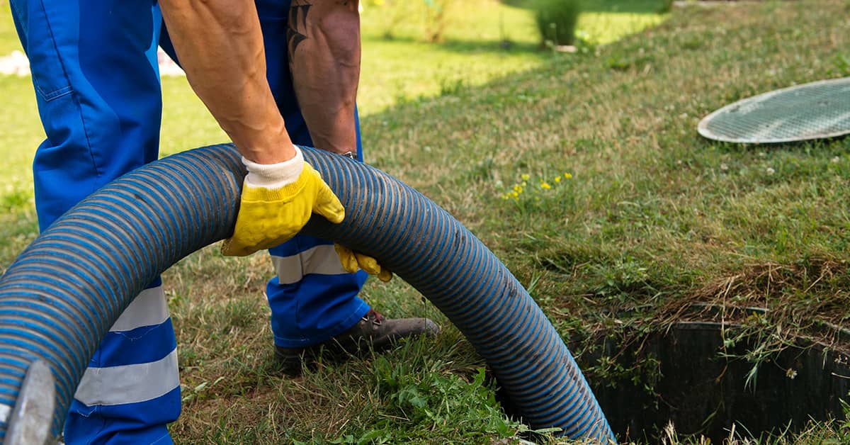 Technician emptying a septic tank with a large hose in a grassy area.