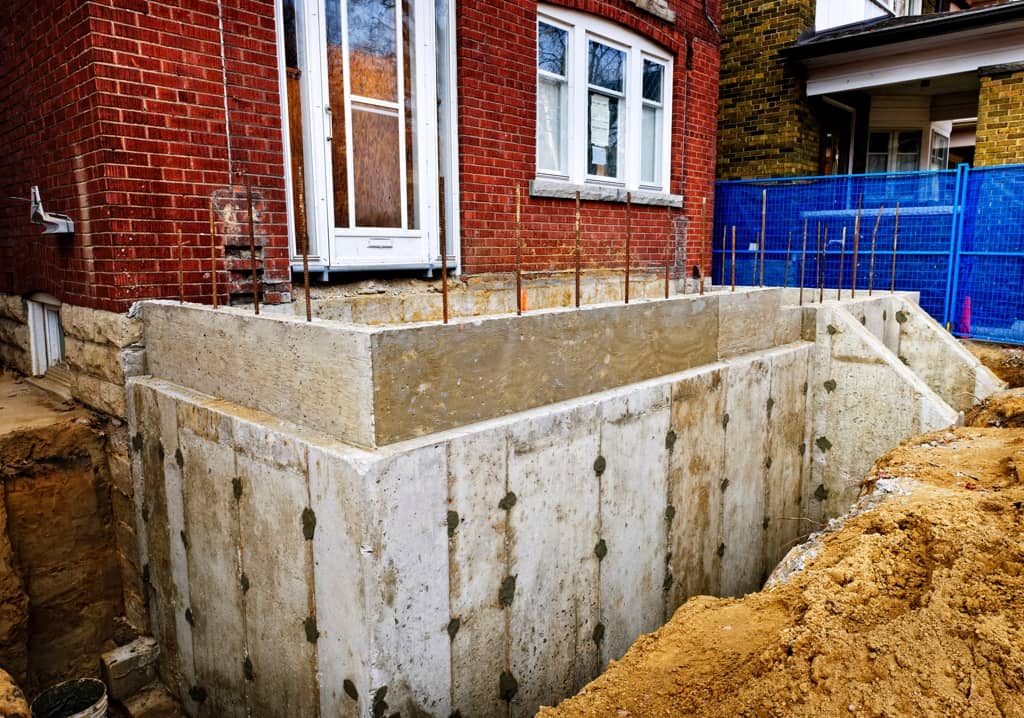Foundation work for property extension with exposed concrete and brick structure.