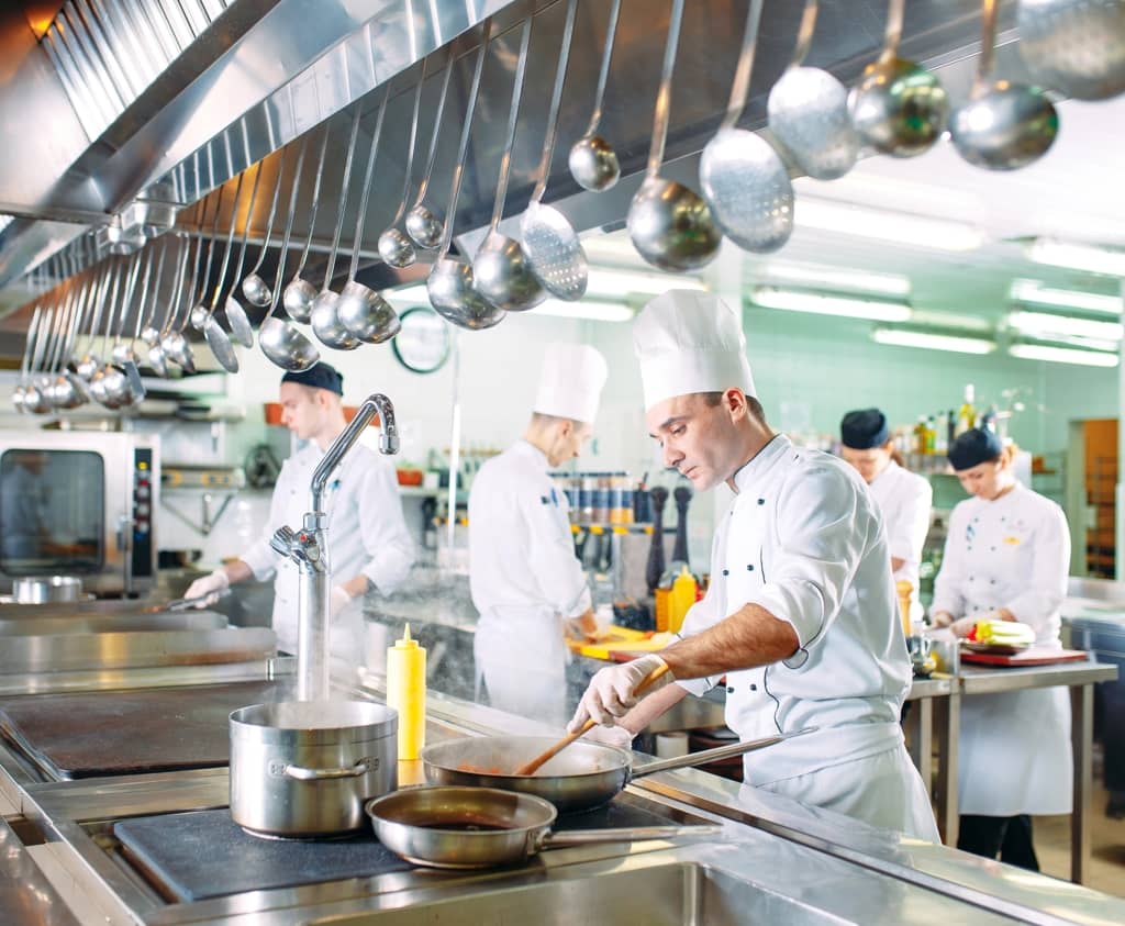 Chefs working in a busy restaurant kitchen with various kitchen utensils and cooking equipment.