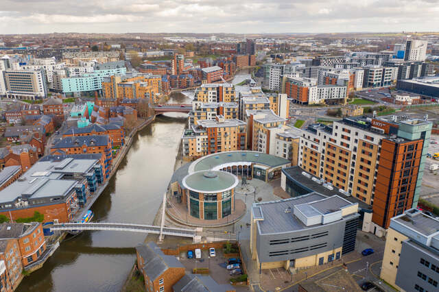 Aerial view of Leeds city centre featuring the River Aire, modern apartments, and business buildings. Unblockers.net offers professional drain unblocking services in Leeds