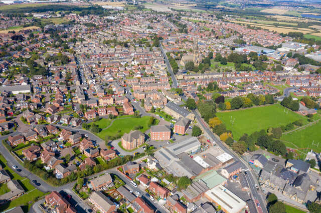 Aerial photo of Ossett, West Yorkshire, with houses, church spire, and green parks visible. Unblockers.net offers expert drain unblocking services throughout Ossett with transparent pricing and rapid response.